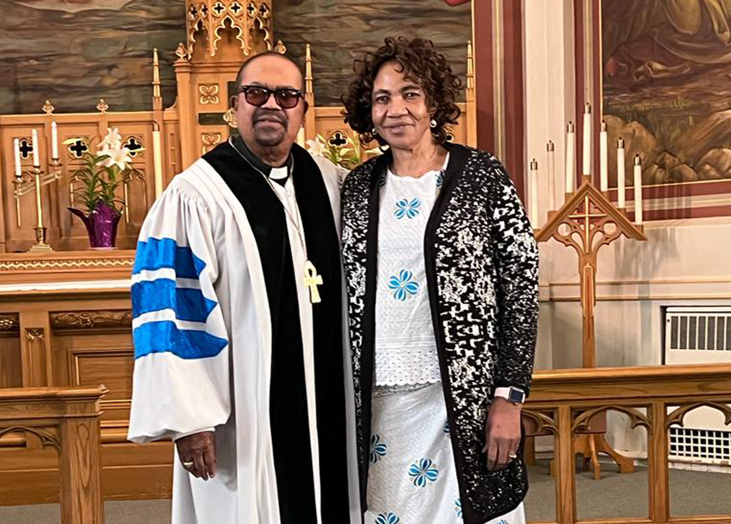 A pastor in white vestments and a woman standing together in a church sanctuary