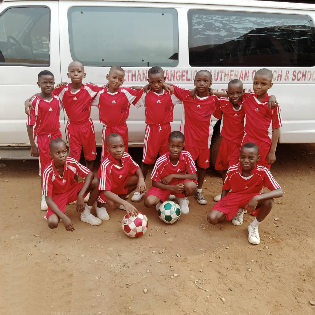The school football team in red kit in front of the Bethany Lutheran bus