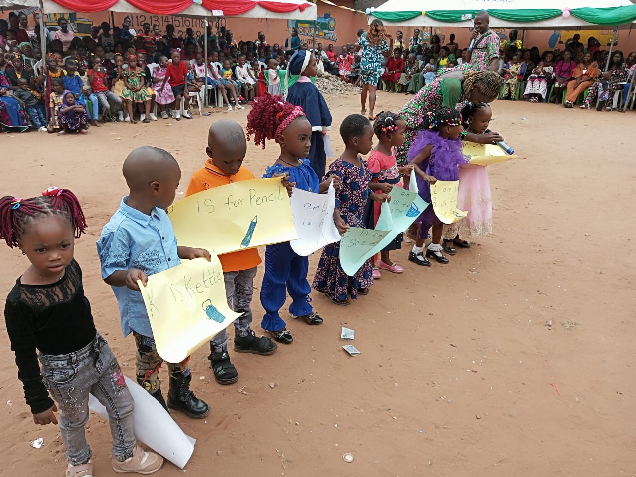 Young pupils holding up certificates at a school ceremony, families watching